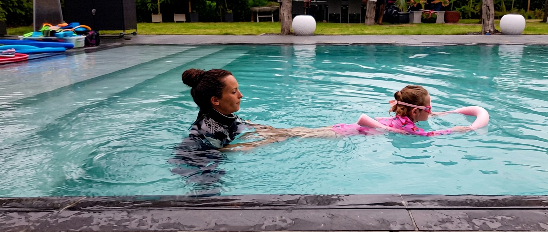 Inez Schoofs staat in het water en begeleidt een jong meisje dat drijft